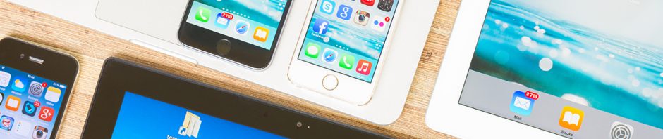 Brand new Apple iPhones 6 and 5S sit on a Macbook keyboard surrounded by iPad tablets and various other Apple devices.